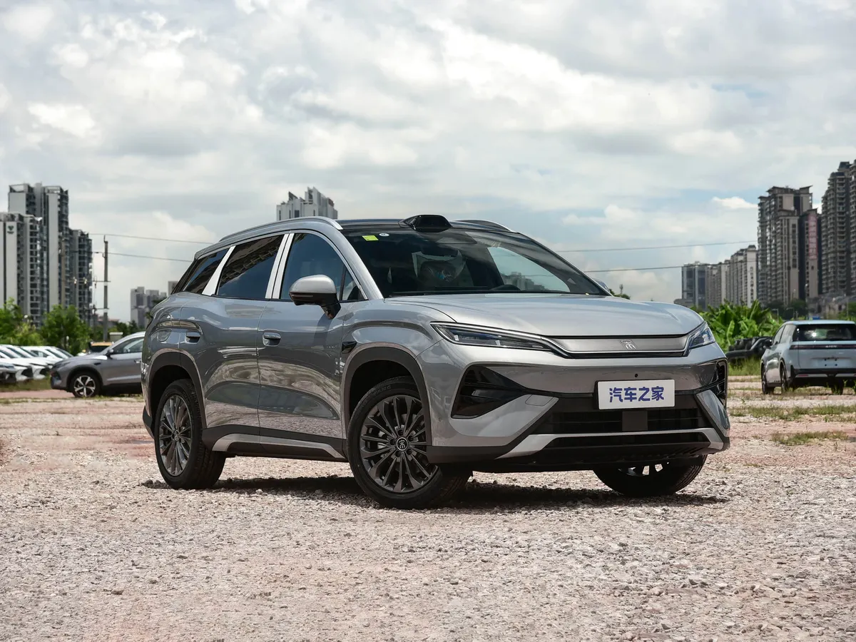 Серый BYD Song Ultra на гравийной площадке на фоне городских домов и облачного неба