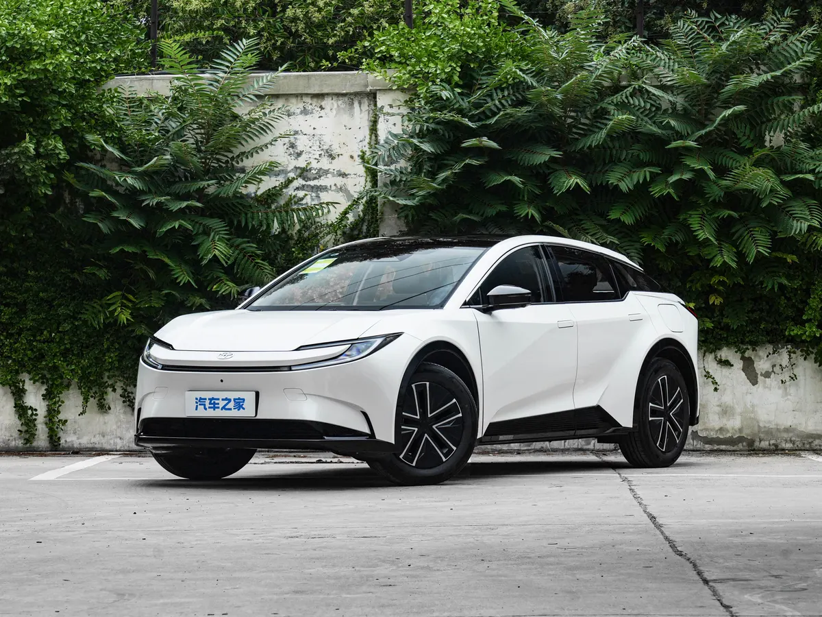 Белый кроссовер Toyota с обтекаемым кузовом на парковке у стены, увитой зеленью