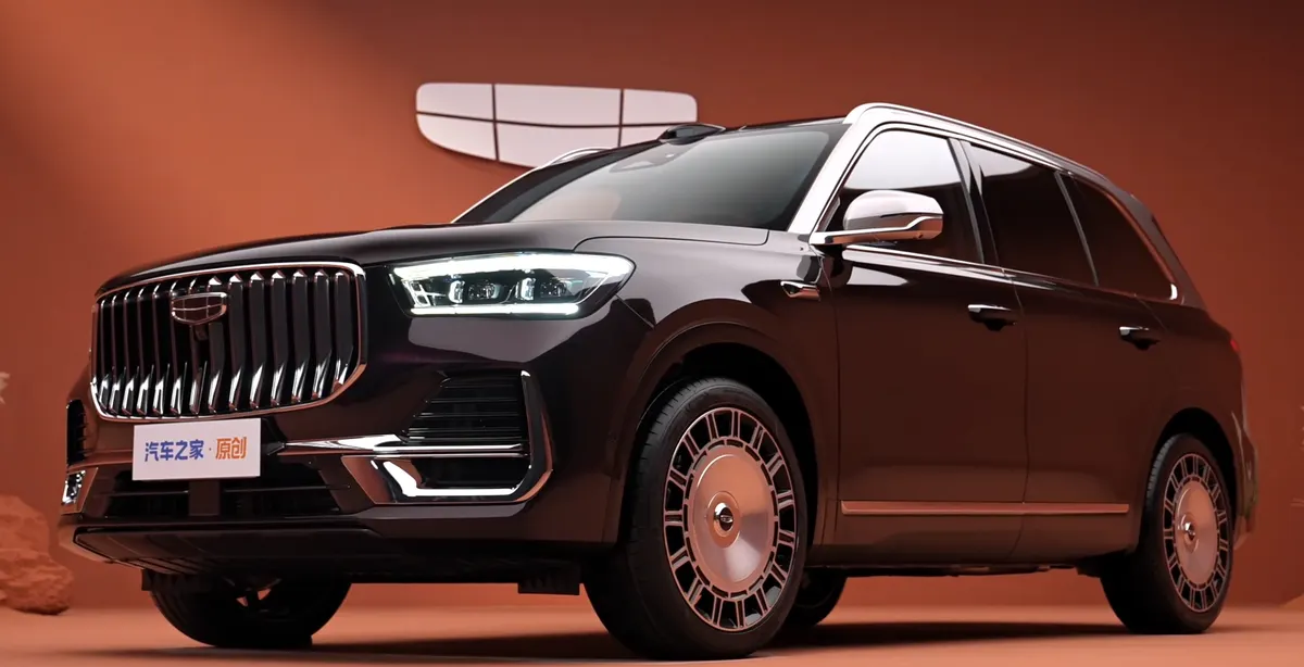 Тёмный Geely Xingyue L PLUS спереди в три четверти на оранжевом фоне: вертикальная хромированная решётка и диски