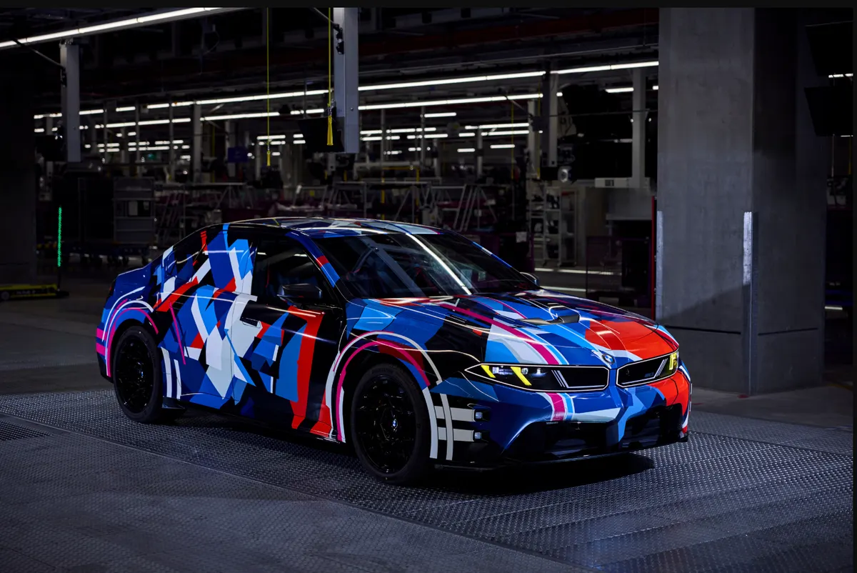 BMW M3 в пёстрой сине-красной камуфляжной плёнке на заводском полу, вид спереди в три четверти
