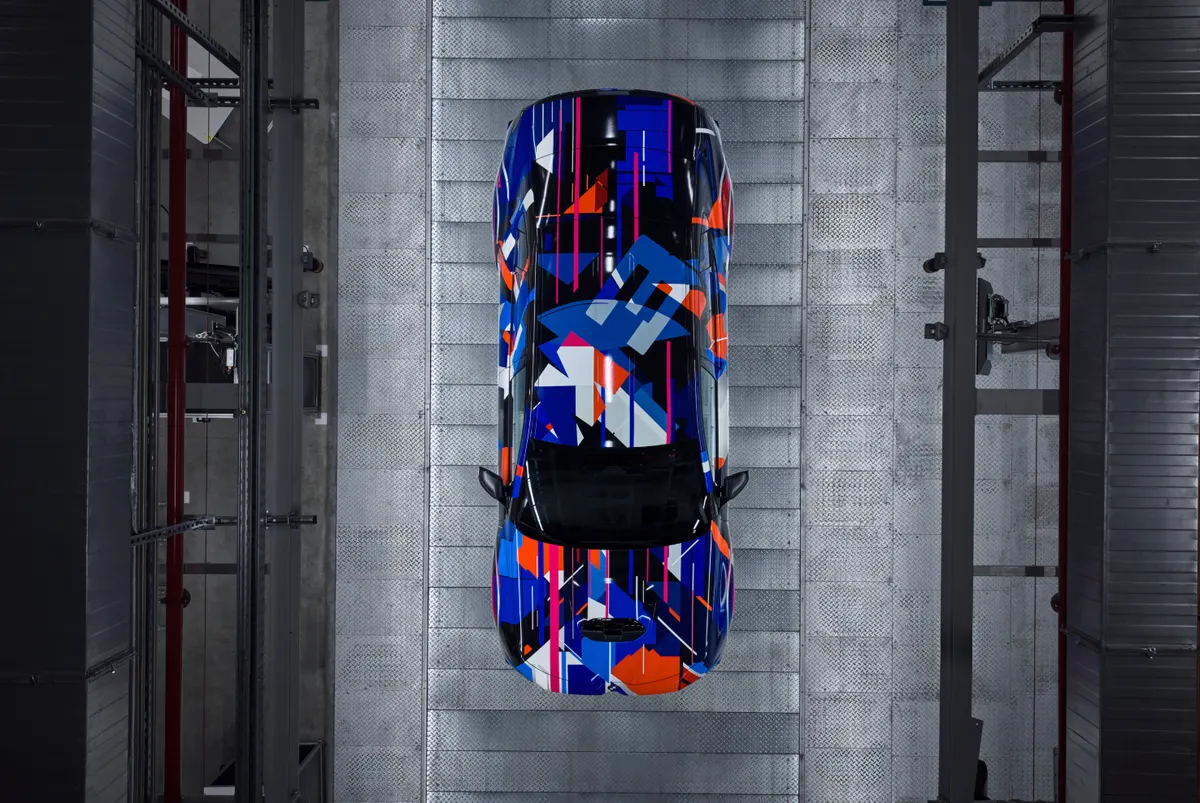 Вид сверху на BMW M3 в сине-оранжево-чёрной камуфляжной плёнке на металлическом полу цеха