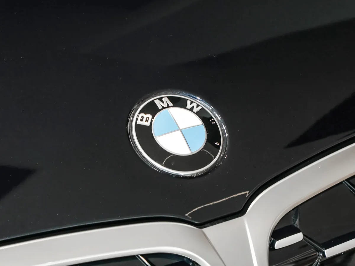 Круглая эмблема BMW на чёрном капоте над серебристой решёткой радиатора; у края капота заметна тонкая царапина