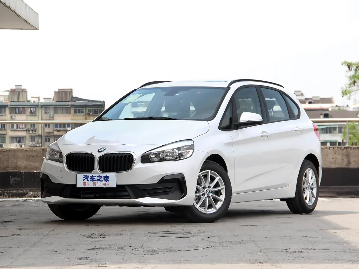 Белый BMW 2 Series Active Tourer, вид спереди сбоку, на парковочной площадке на фоне жилых домов