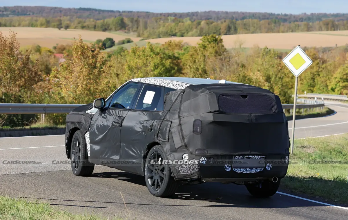 Kia Sportage в маскировке сзади сбоку: закрытая задняя часть, выхлопная труба, дорожный знак на обочине
