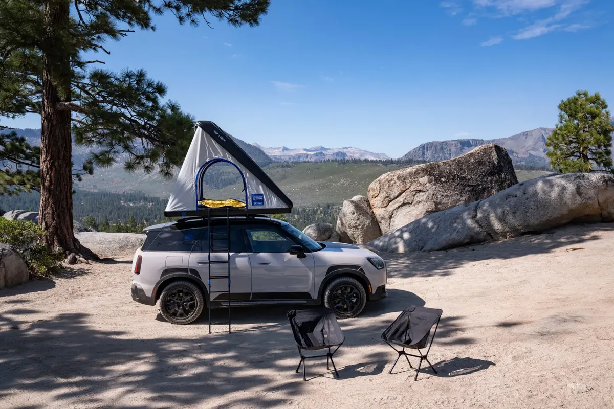 MINI Countryman с палаткой на крыше и лестницей на стоянке в горах, рядом два раскладных стула