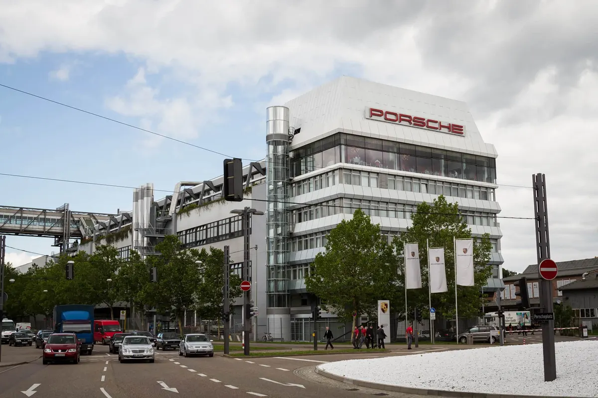Офисное здание Porsche с красной надписью на городской улице, на дороге движутся автомобили