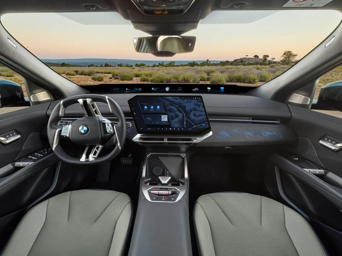 Салон BMW iX4: руль, широкий дисплей под лобовым стеклом, центральный экран и светло-серые сиденья