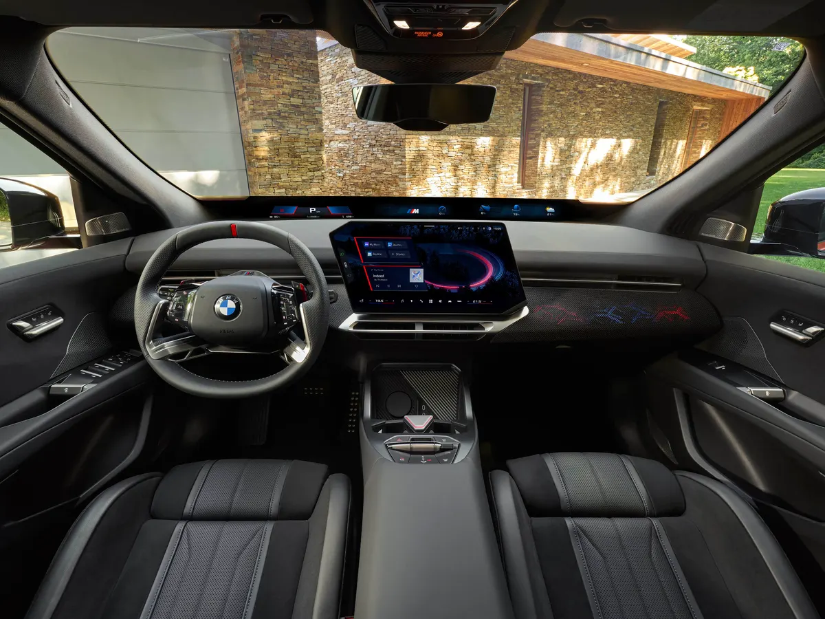 Салон BMW iX4 в спортивной версии M: чёрная отделка, центральный экран и цветная подсветка панели