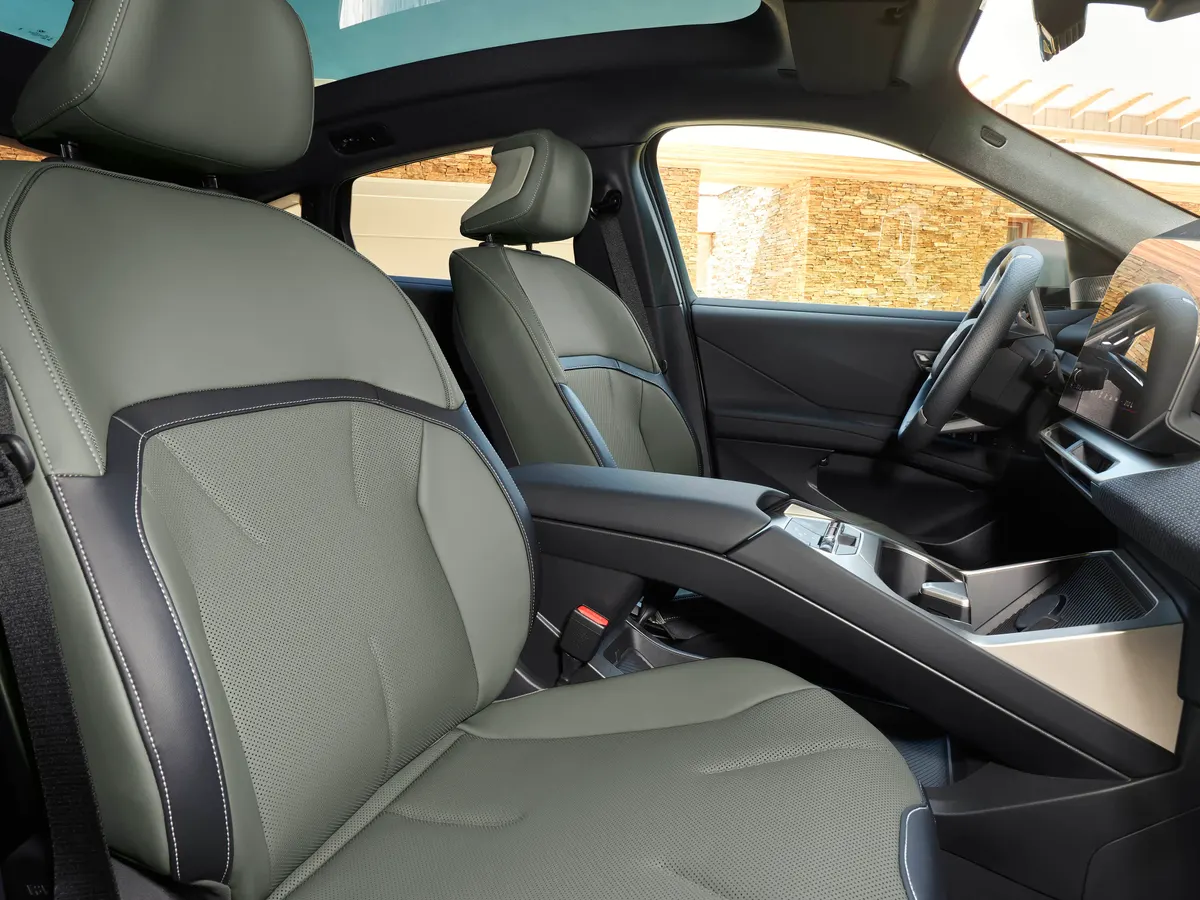 Передние сиденья BMW iX4 из серо-зелёной кожи с перфорацией и тёмными вставками, виден центральный тоннель