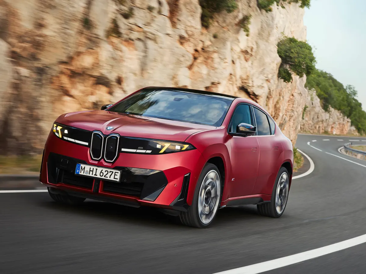 Красный BMW iX4 едет по горной дороге вдоль скалы, вид спереди в три четверти