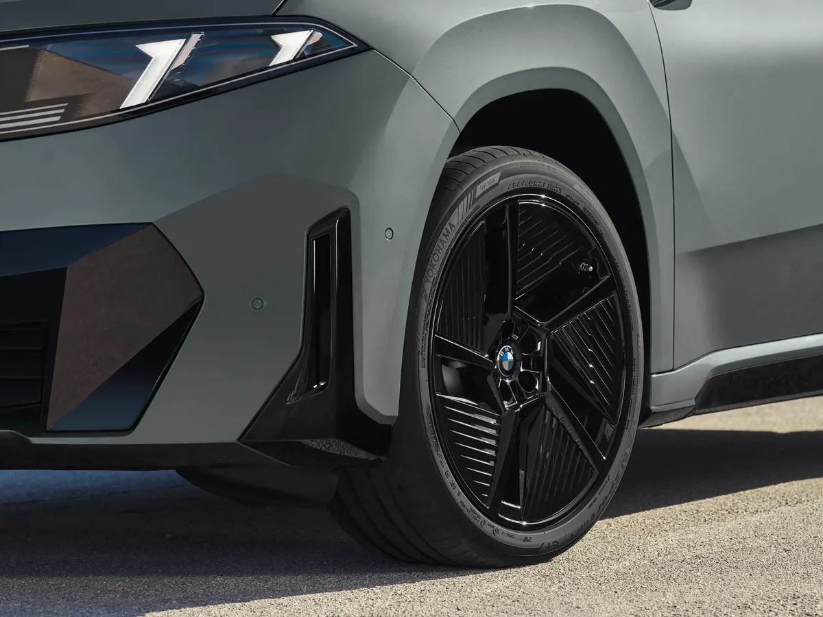 Передняя часть BMW iX4 крупным планом: чёрный литой диск, фара с Г-образной подсветкой и воздухозаборник