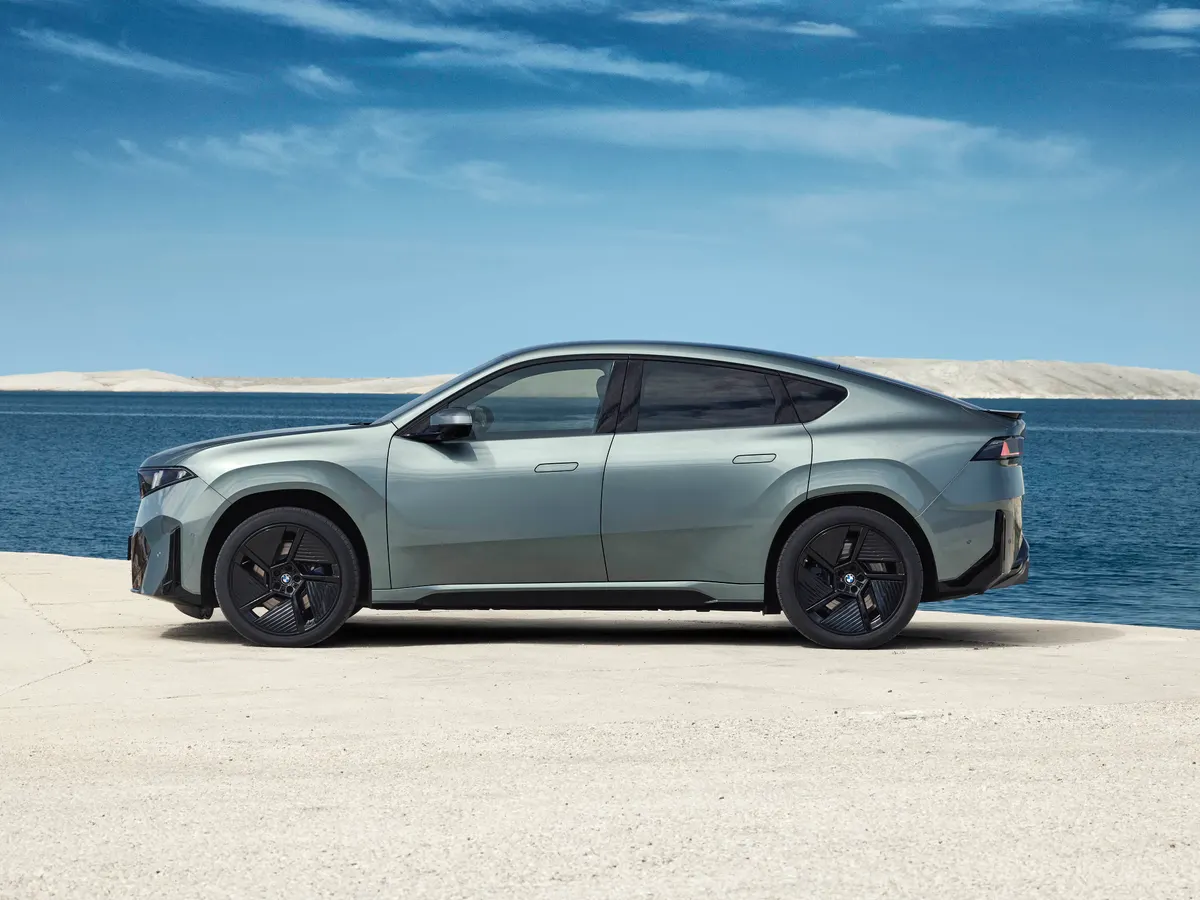 Серо-зелёный BMW iX4 в профиль на фоне моря и светлого берега