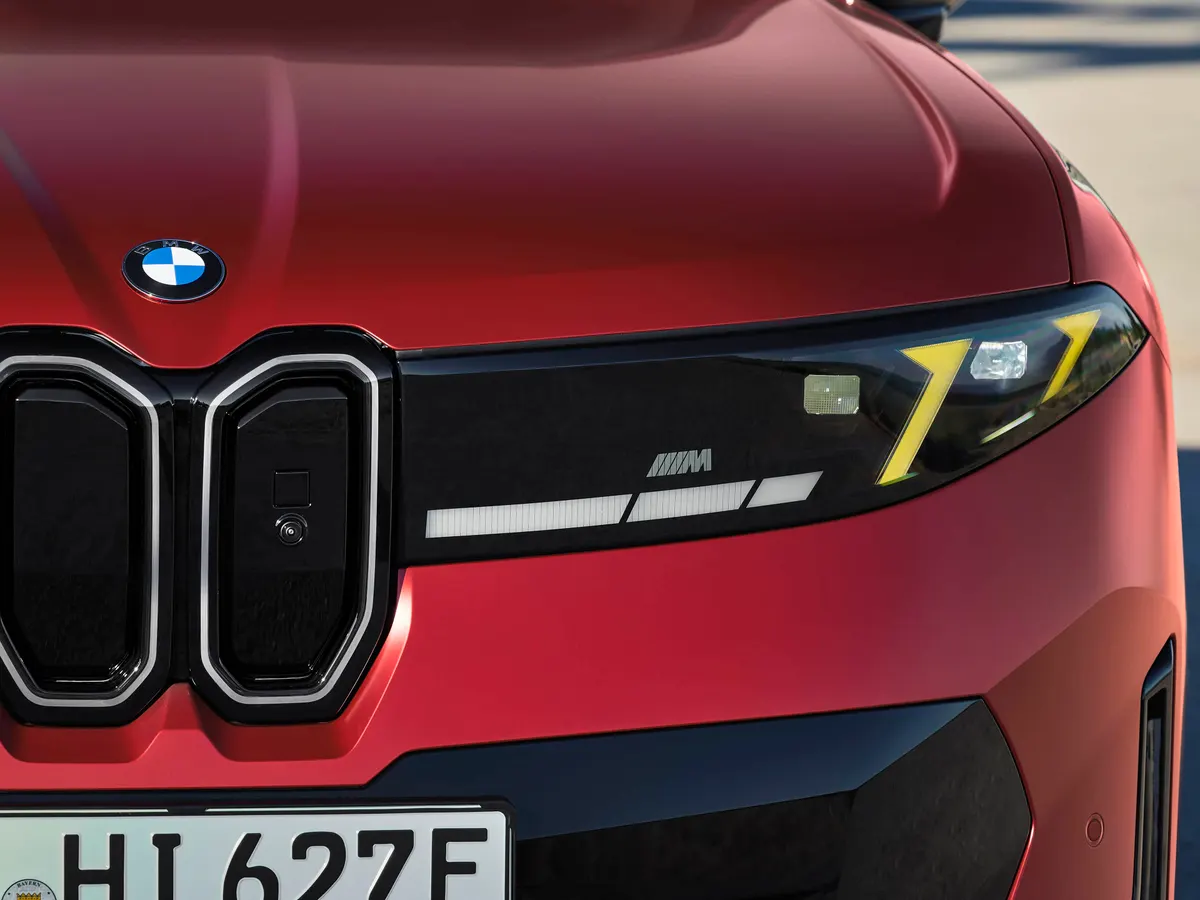 Фара красного BMW iX4 с жёлтыми элементами подсветки и значком M, рядом ноздри решётки радиатора