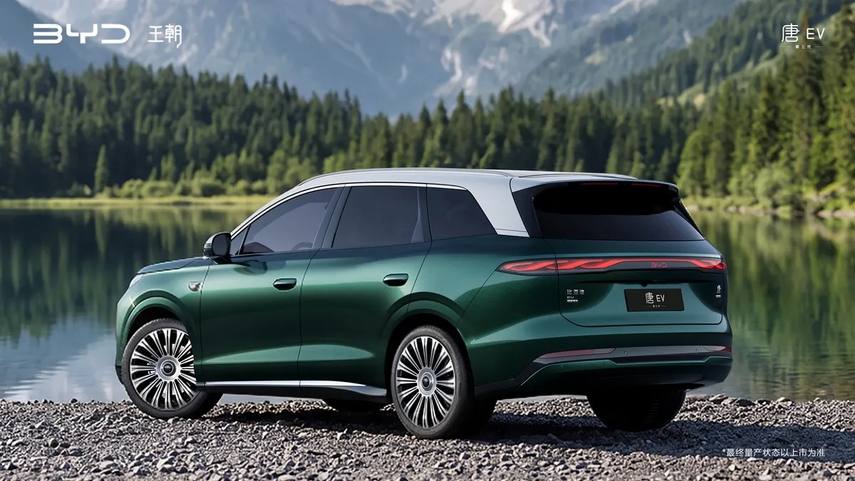 Зелёный BYD Tang сзади на галечном берегу горного озера, сплошная полоса задних фонарей, хвойный лес