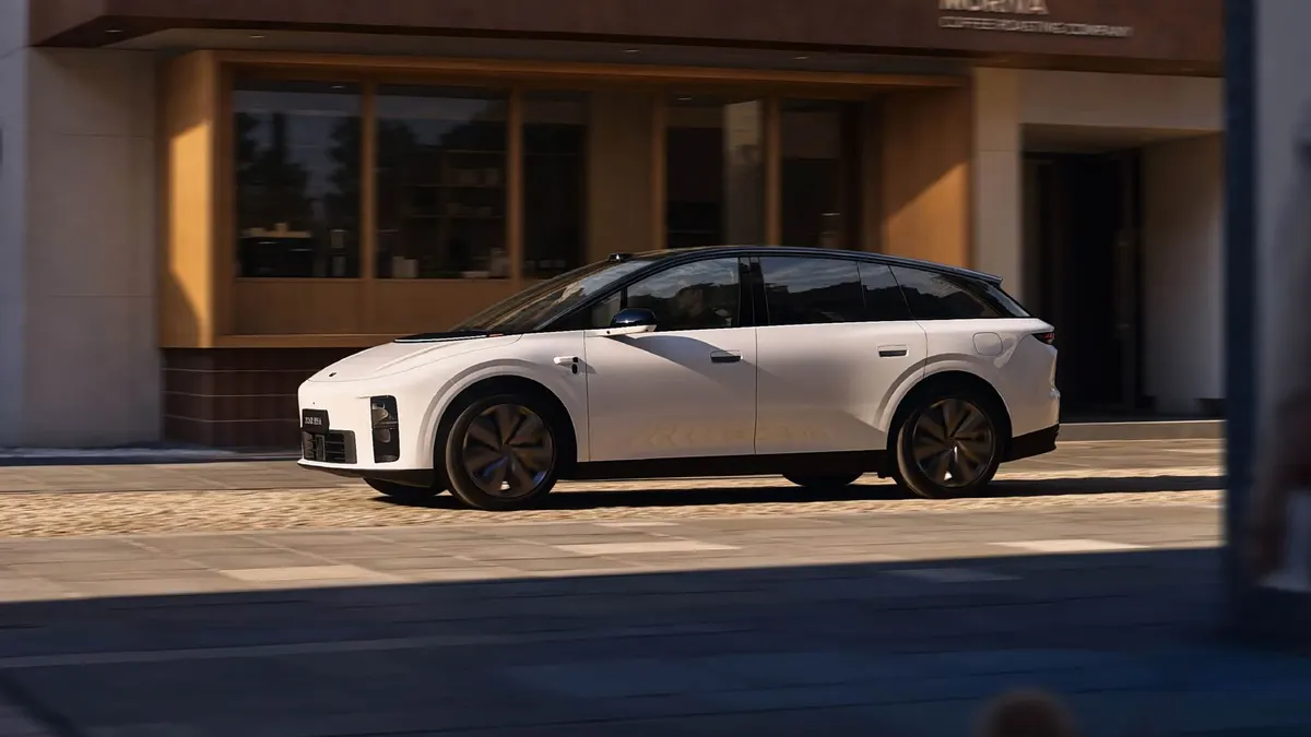 Белый Li Auto i6 едет по городской улице мимо здания с деревянной отделкой фасада