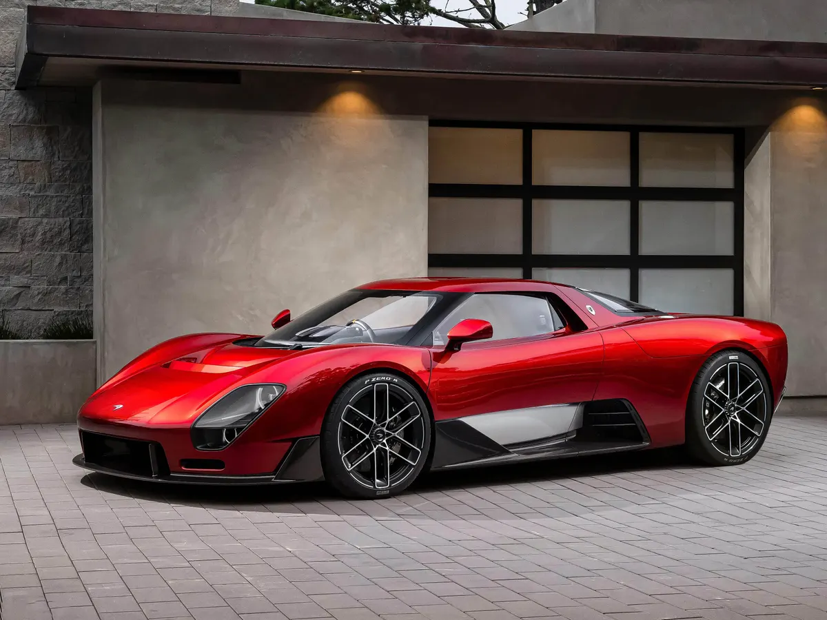 Красный спорткар McLaren с чёрными дисками в три четверти спереди у здания с каменной кладкой