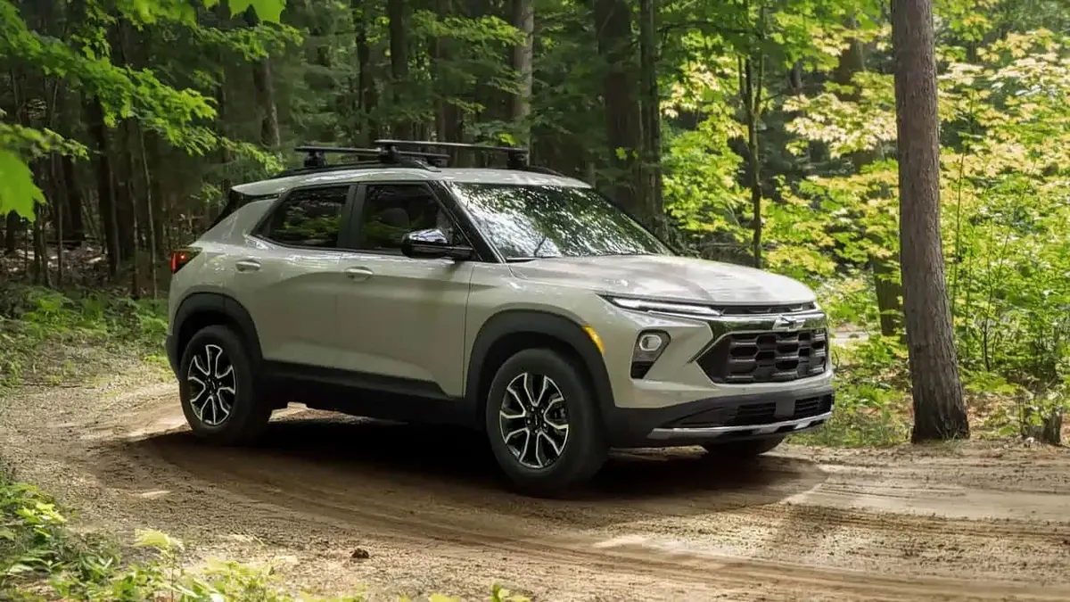Chevrolet Trailblazer светло-серого цвета с рейлингами на крыше едет по лесной грунтовой дороге