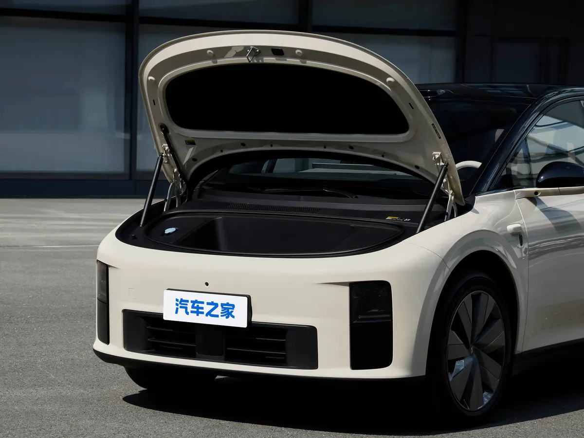 Светлый Li Auto с открытым передним багажником под капотом, на асфальте у стеклянного здания