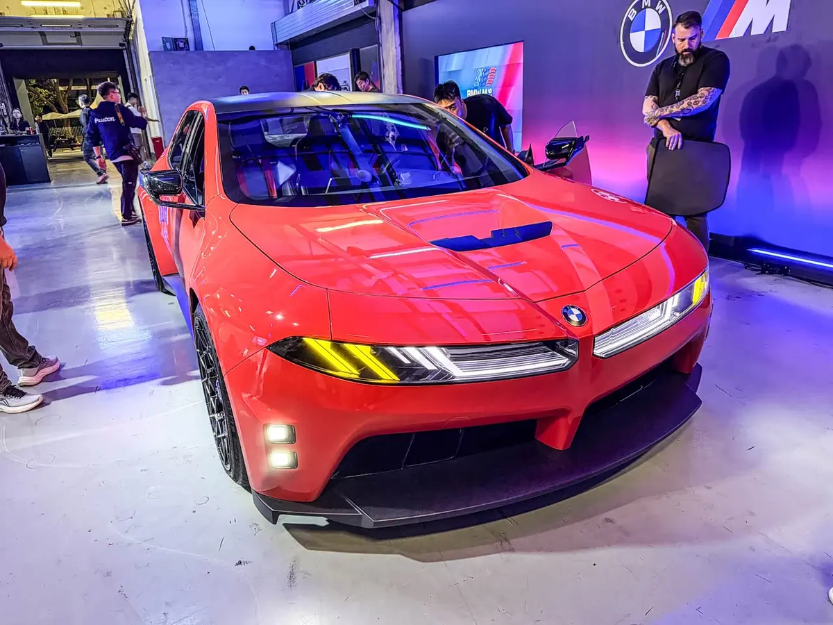 Красный концепт BMW M Concept Neue Klasse на выставочной площадке на фоне стены с логотипами BMW и M