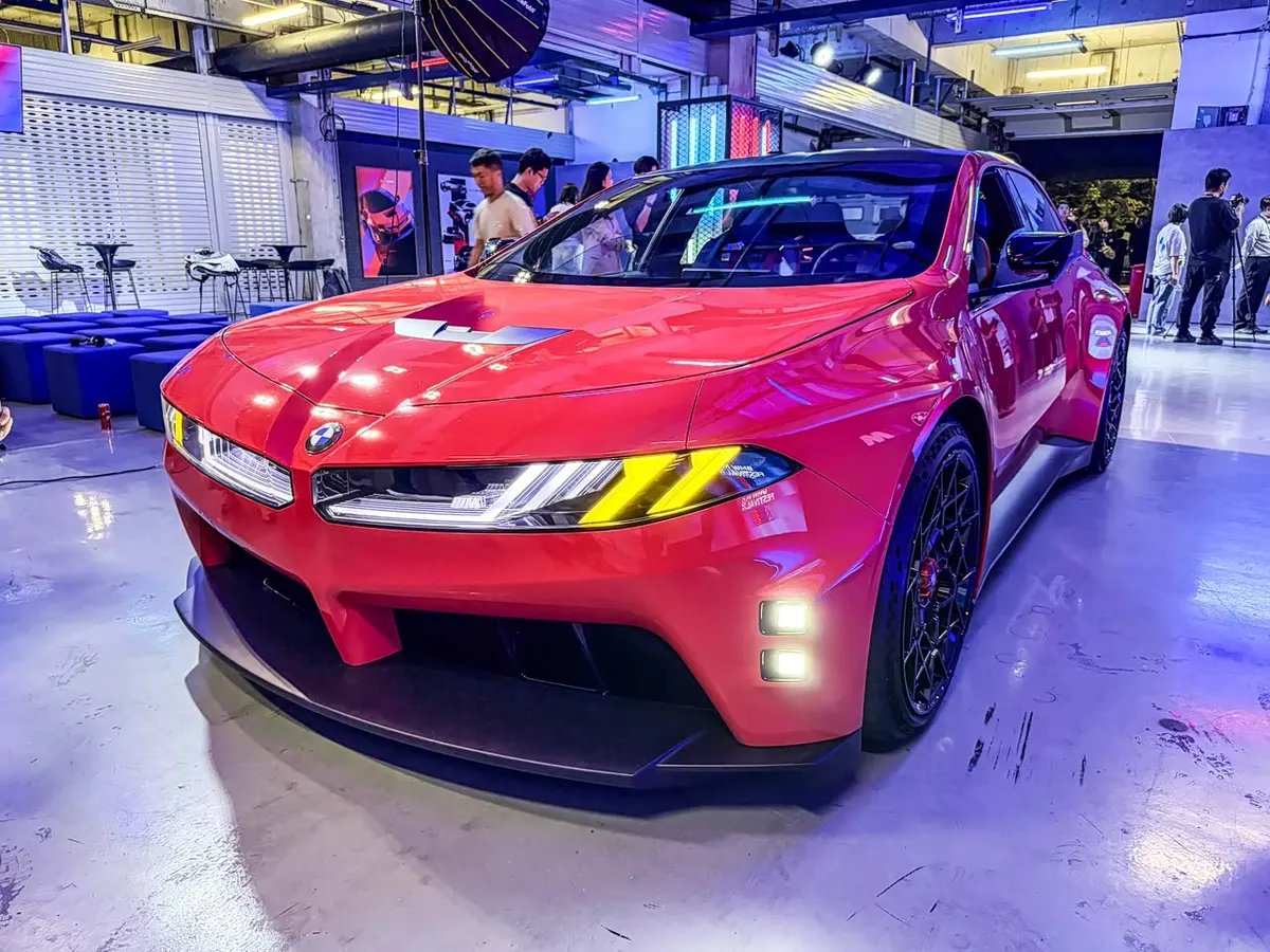 Красный BMW M Concept Neue Klasse спереди слева в зале, на заднем плане посетители выставки