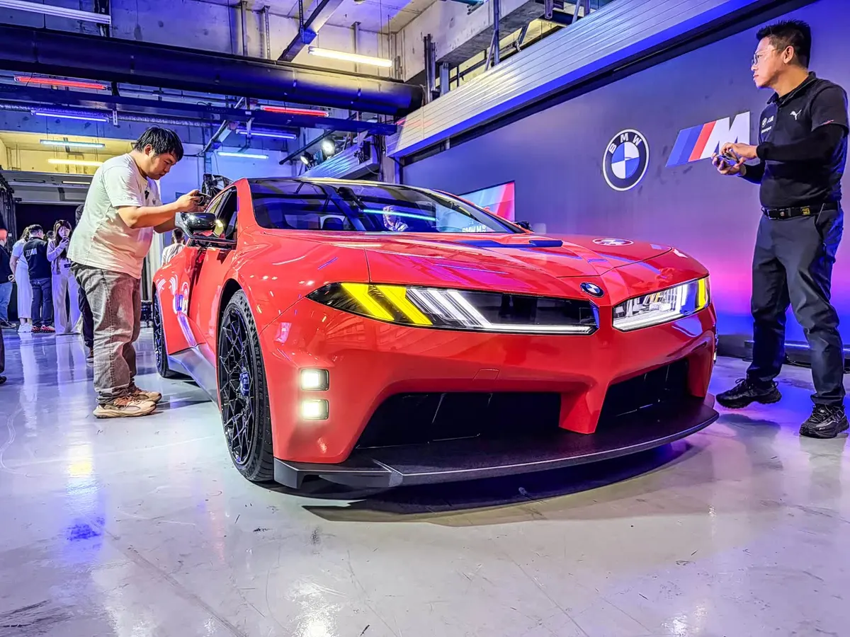 Красный BMW M Concept Neue Klasse спереди: посетитель снимает машину на телефон