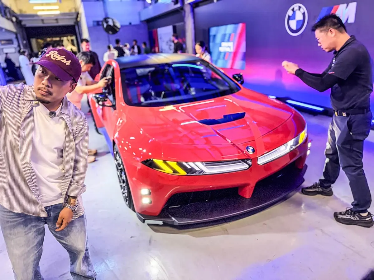 Передняя часть красного BMW M Concept Neue Klasse, рядом посетители с телефонами