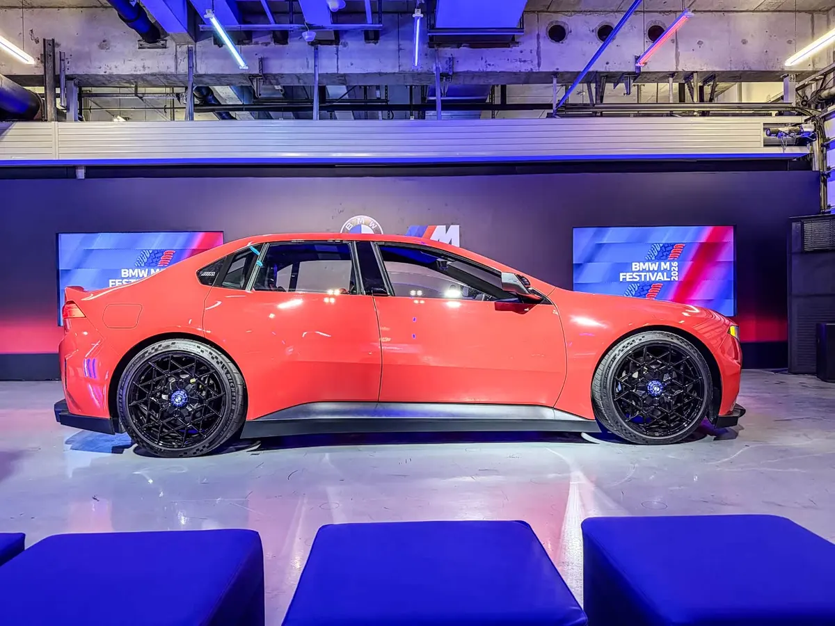 BMW M Concept Neue Klasse сбоку: красный кузев, чёрные литые диски, экраны BMW M Festival 2026