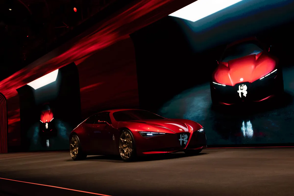 Красный концепт Alfa Romeo Cuorerosso на тёмной сцене, на экранах позади видны его изображения