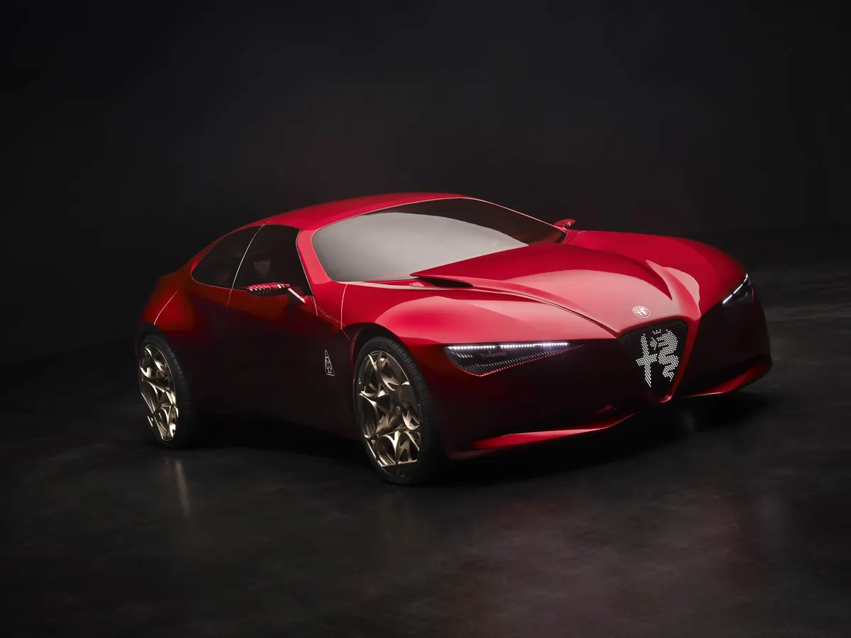 Красный Alfa Romeo Cuorerosso в три четверти спереди на тёмном фоне, бронзовые колёсные диски