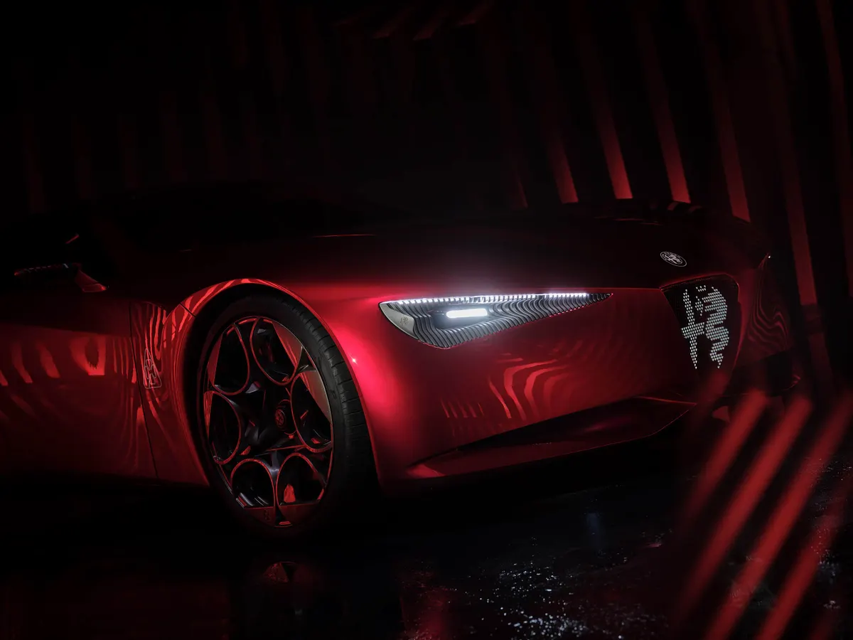 Фара и светящаяся эмблема в решётке Alfa Romeo Cuorerosso крупным планом в красной подсветке