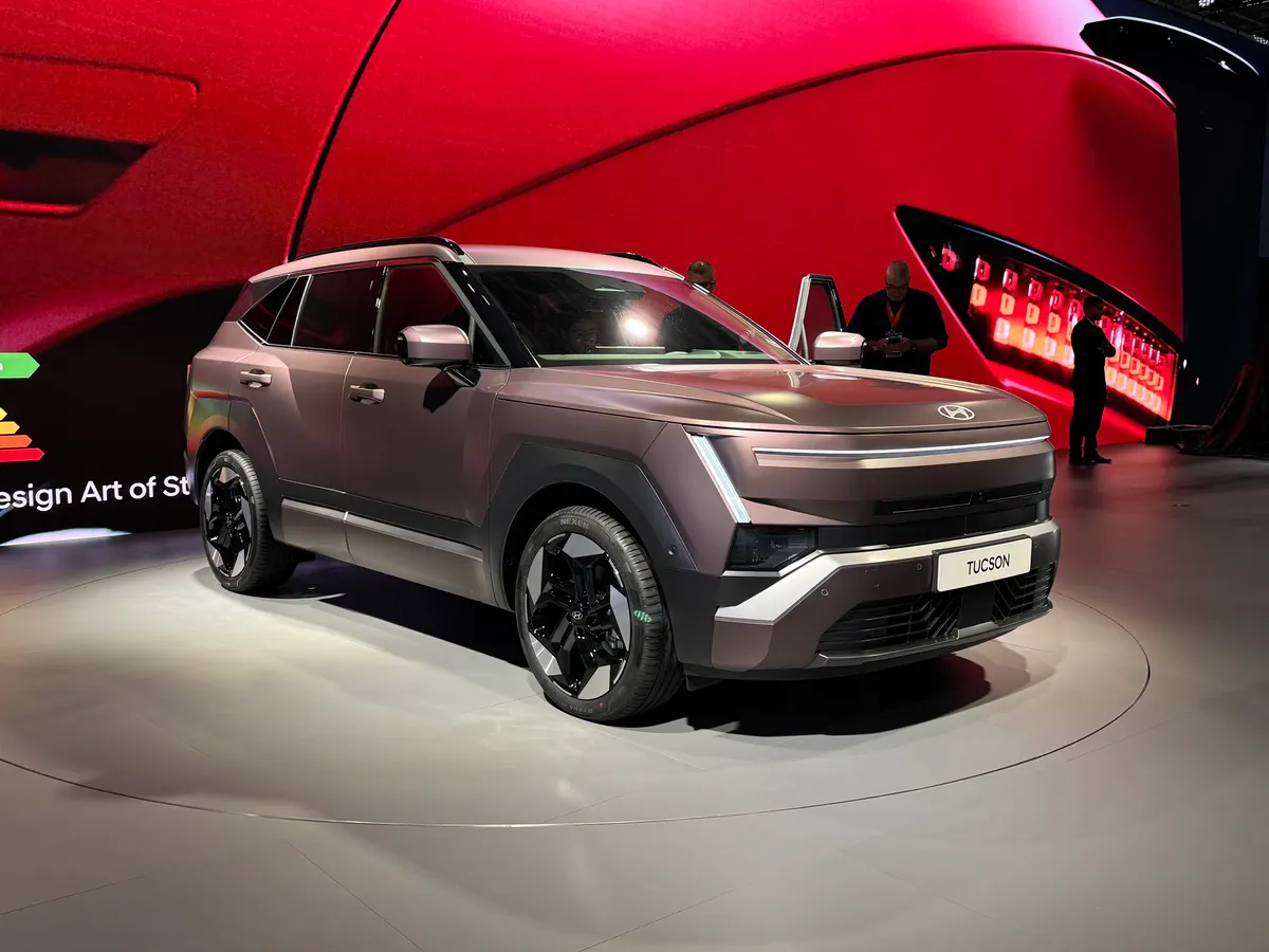 Hyundai Tucson в матово-бронзовом цвете на круглом подиуме на фоне красной стены, вид спереди