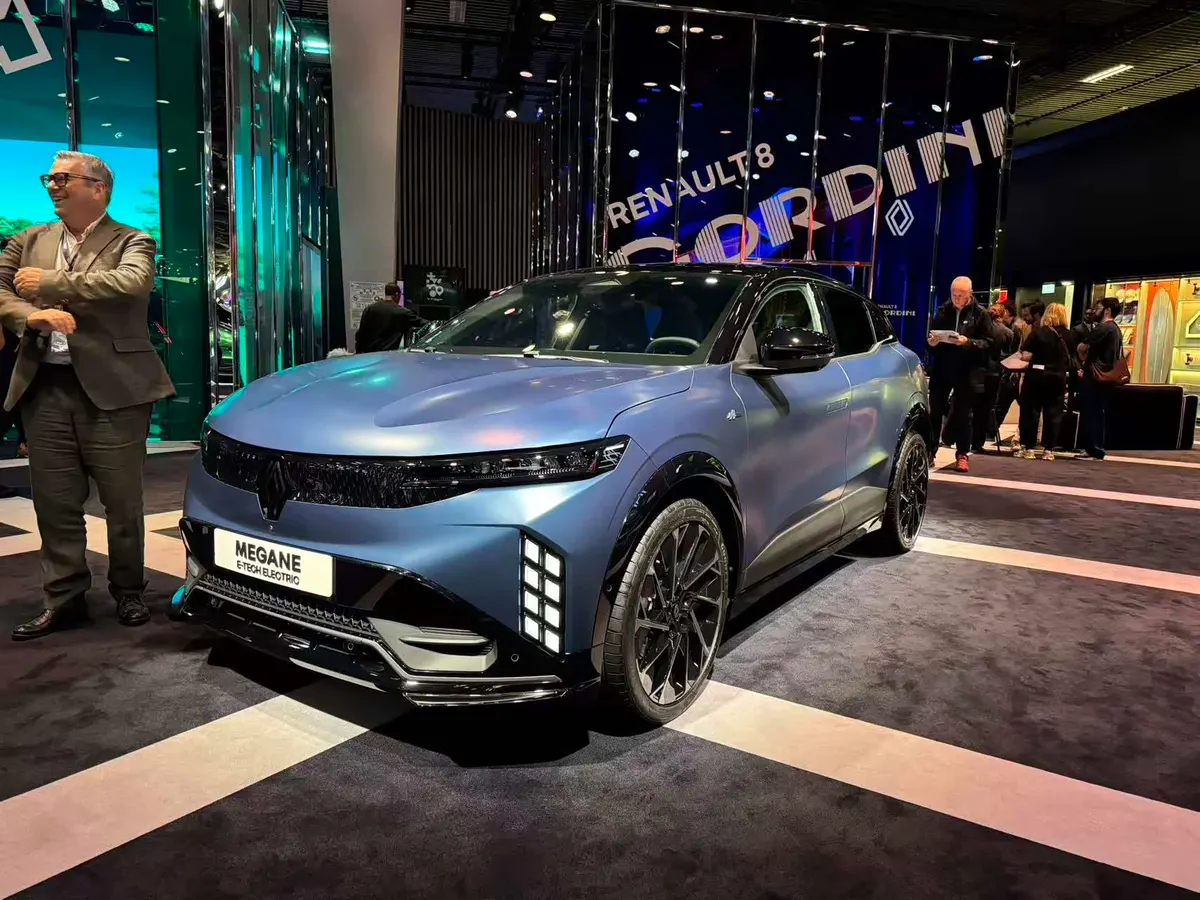 Синий Mégane E-Tech на выставочном стенде Renault, слева улыбающийся мужчина в пиджаке