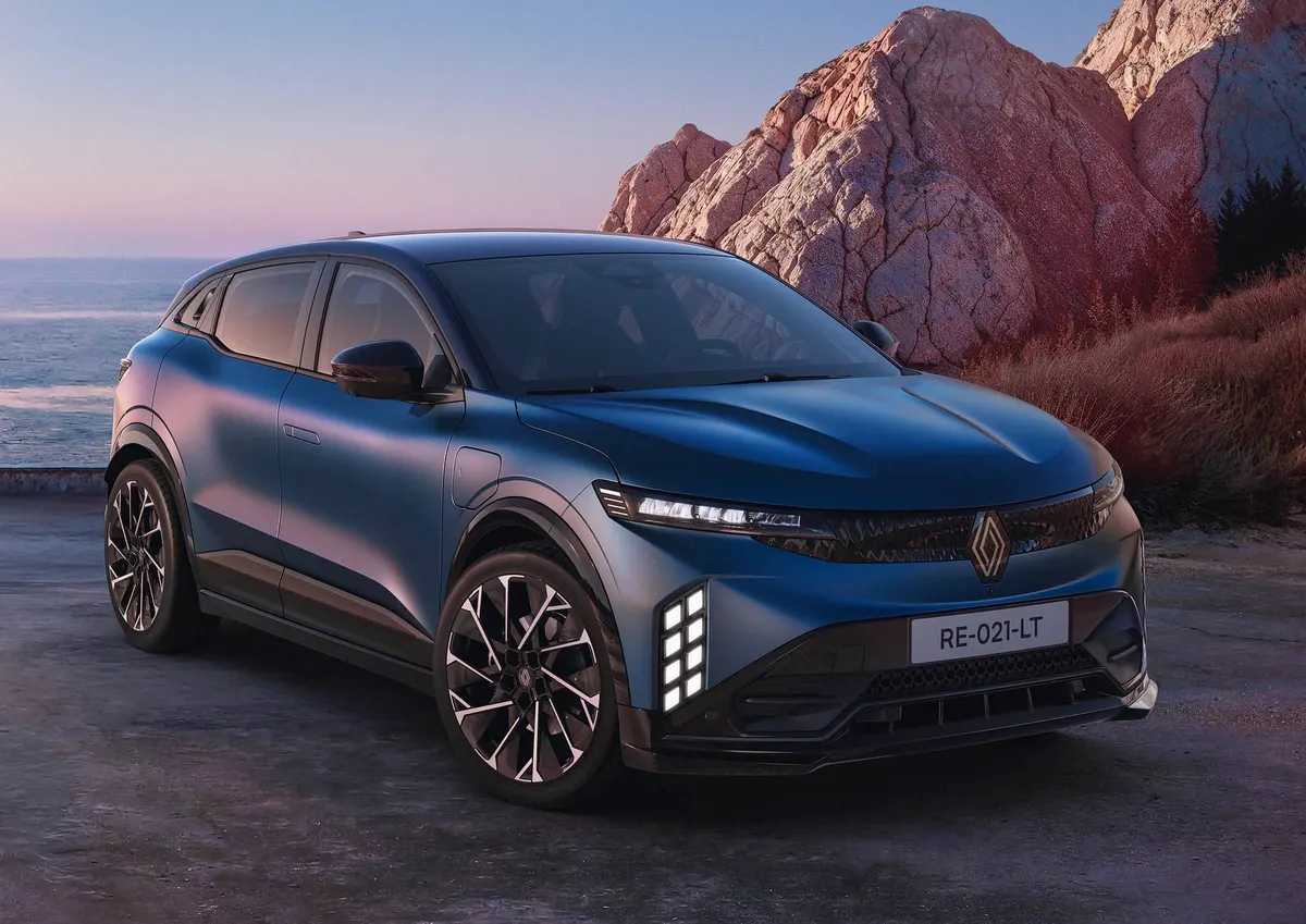 Синий Mégane E-Tech, вид спереди три четверти, на фоне моря и розоватых скал на закате