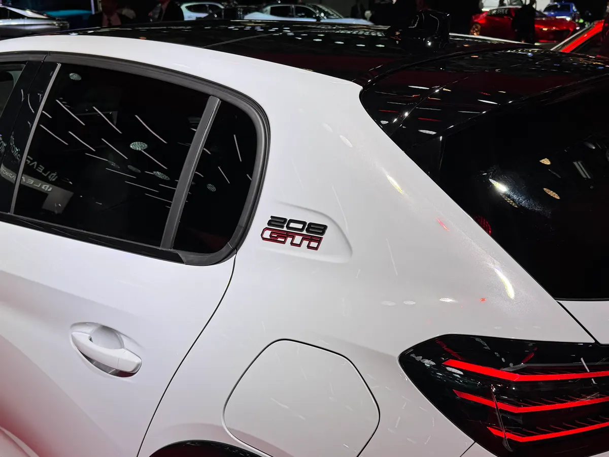 Шильдик 208 GTi на задней стойке белого Peugeot E-208 GTi, рядом ручка двери и лючок зарядки