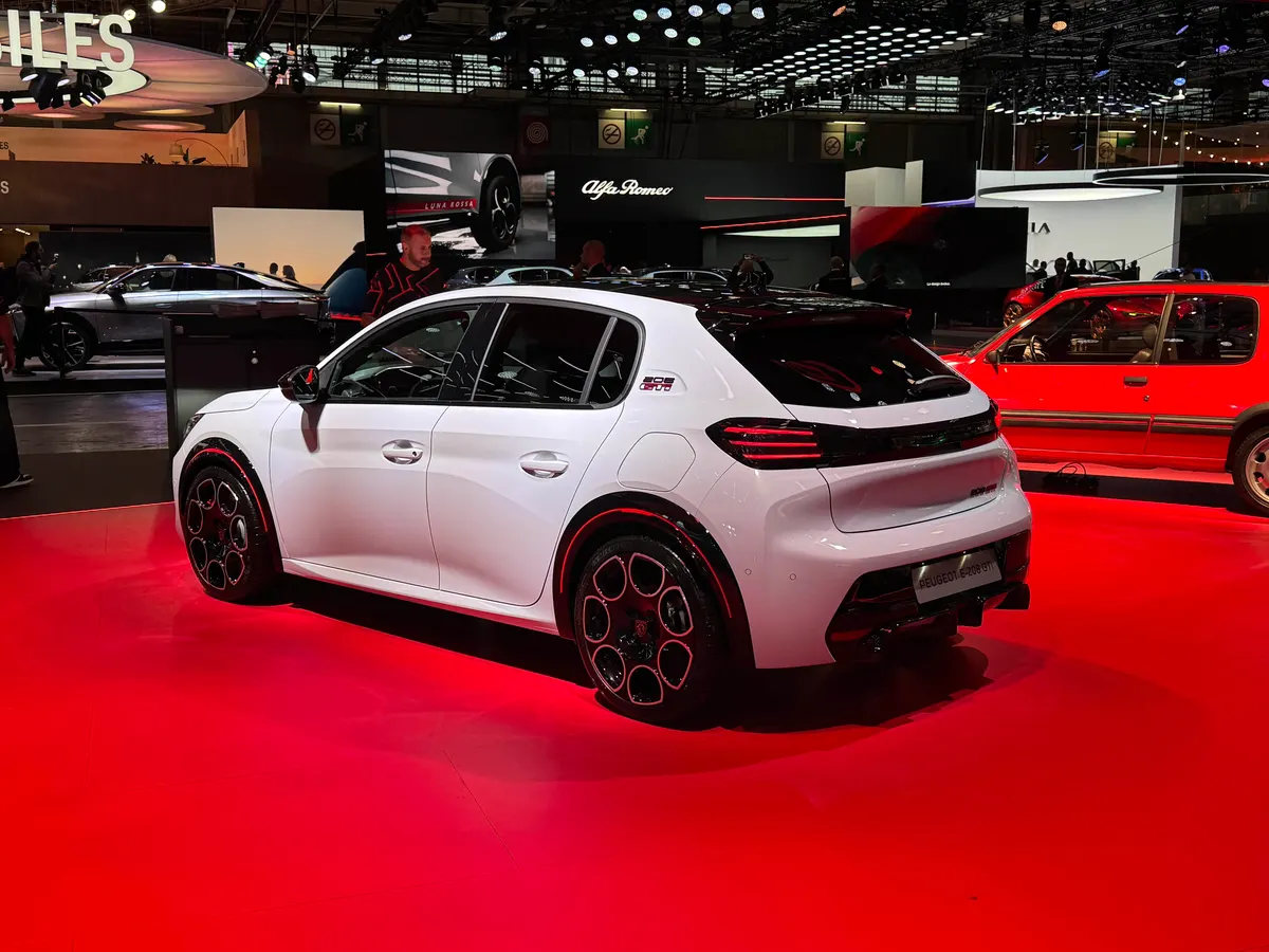 Белый Peugeot E-208 GTi сзади слева: светодиодные красные фонари, чёрные диски, красный старый хэтчбек рядом