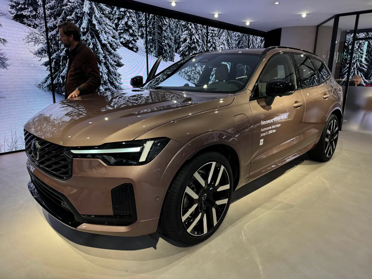 Обновлённый Volvo XC60 бронзового цвета на выставочном стенде, рядом стоит мужчина, на экранах заснеженный лес