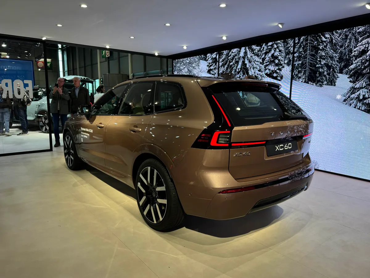 Volvo XC60 в бронзовом цвете сзади и сбоку на выставочной площадке, позади экран с зимним пейзажем