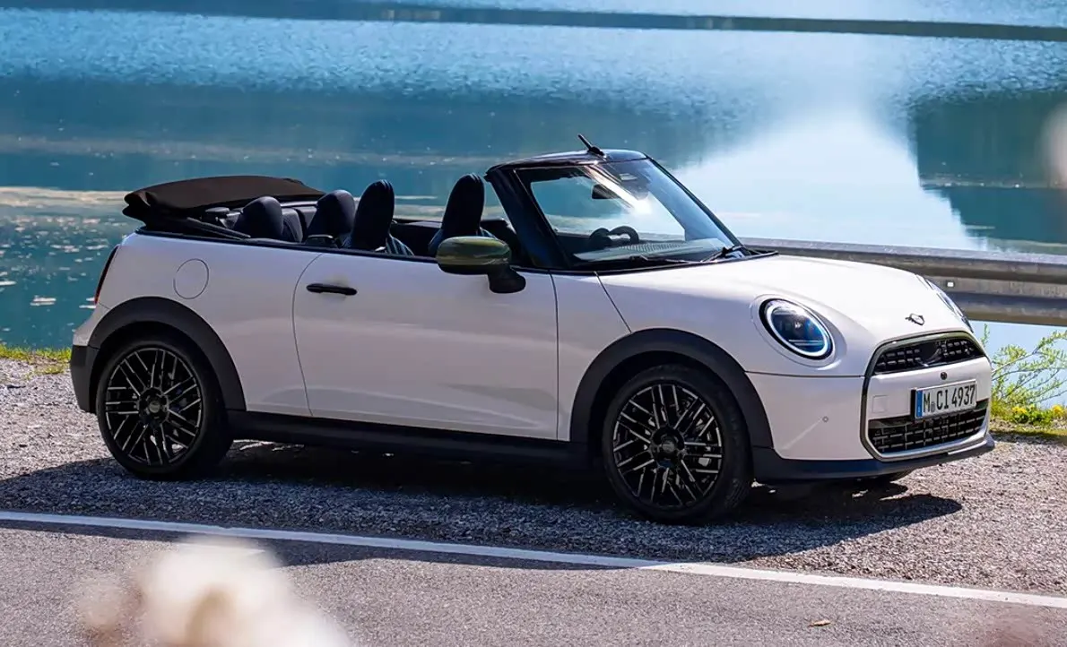 Белый кабриолет MINI с открытым верхом и чёрными дисками на фоне озера