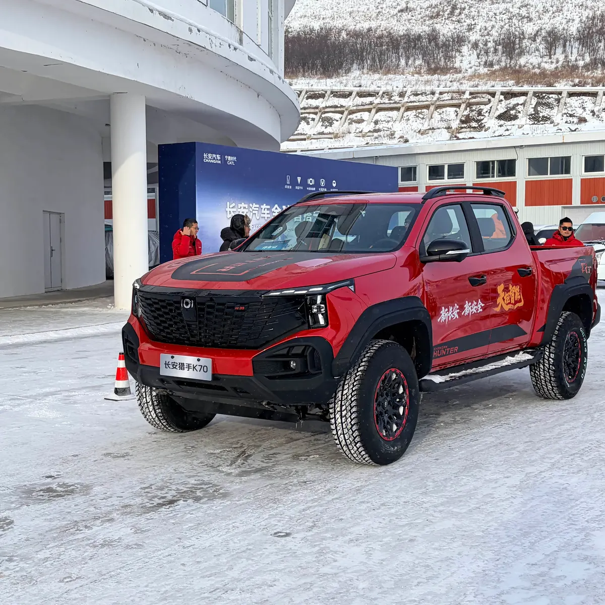 Красный пикап Changan Hunter K70 на заснеженной площадке у белого здания, рядом стоят люди