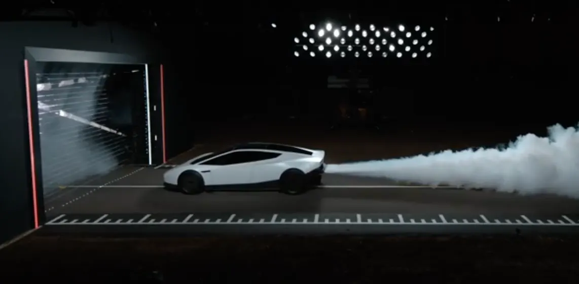 Белый Roadster сбоку в тёмном зале, из задней части вырывается длинная струя дыма