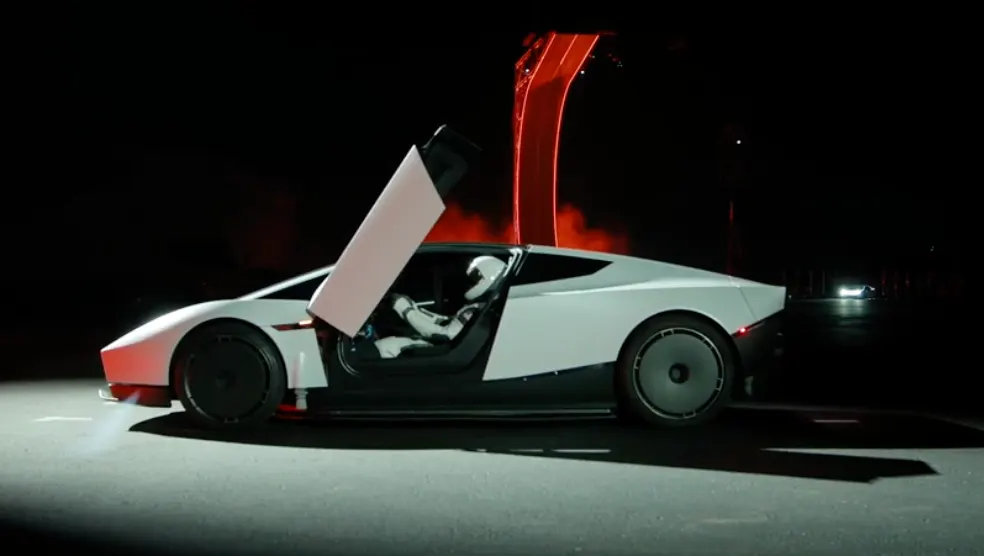 Roadster с поднятой вверх дверью, в кабине человек в белом шлеме, сзади красная подсветка рампы