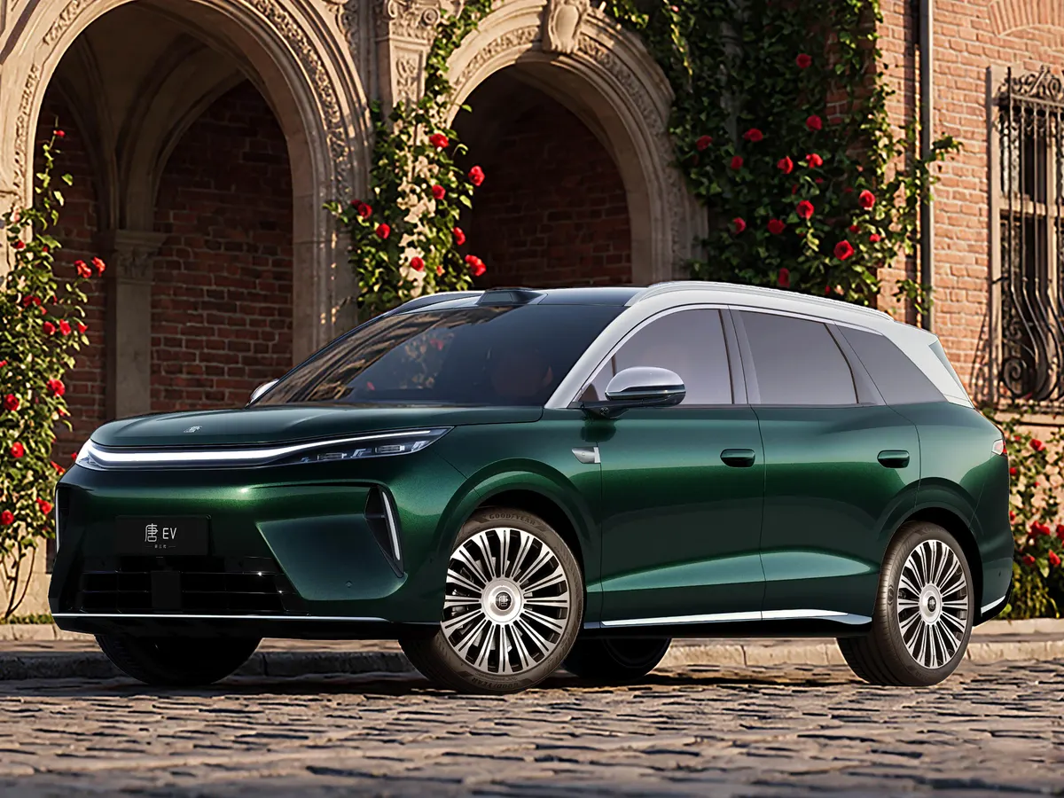 Тёмно-зелёный BYD Tang с серебристой крышей у кирпичной арки с красными розами