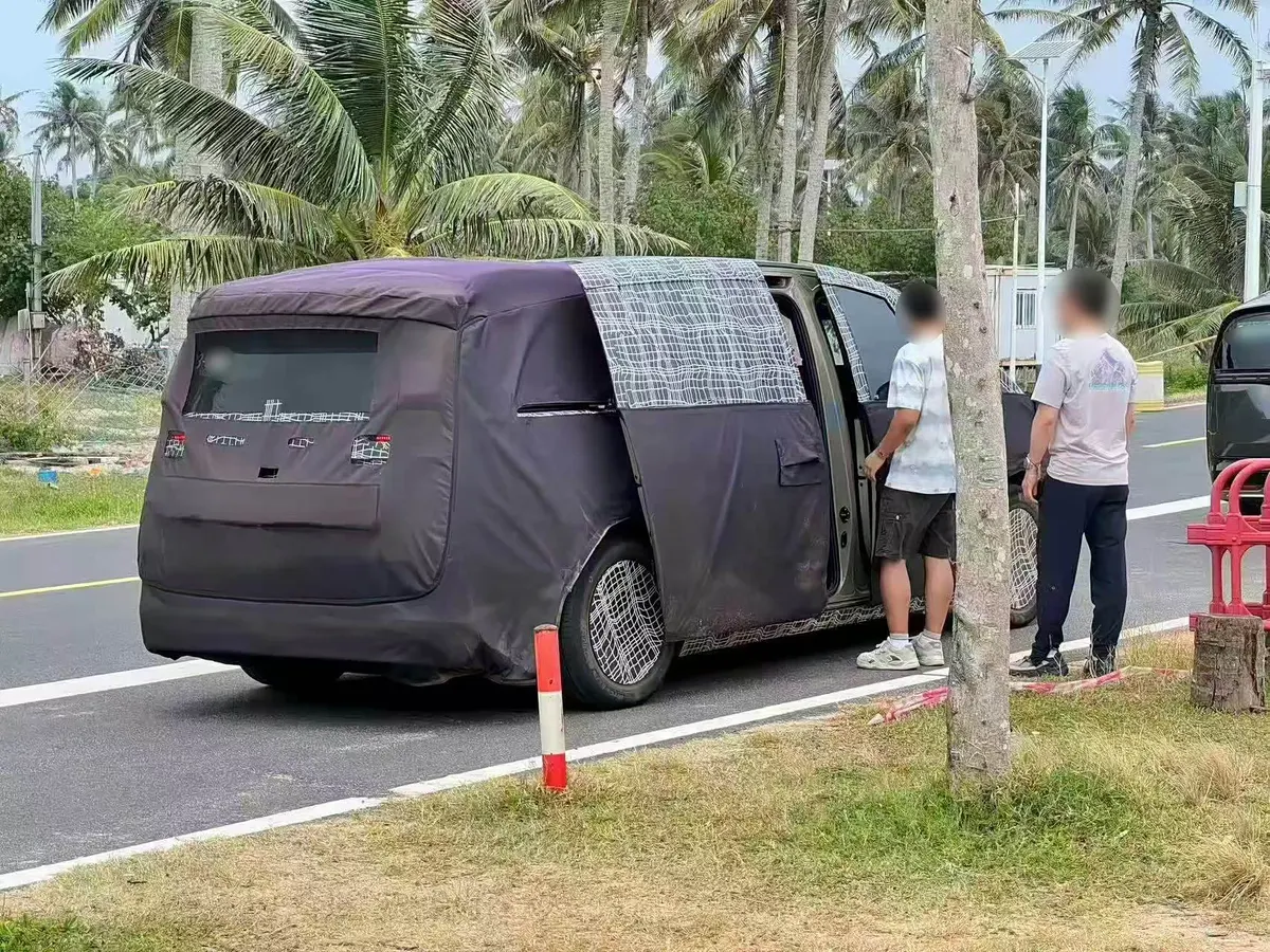 Прототип MPV в маскировочном чехле на дороге среди пальм, сдвижная дверь открыта, рядом двое мужчин