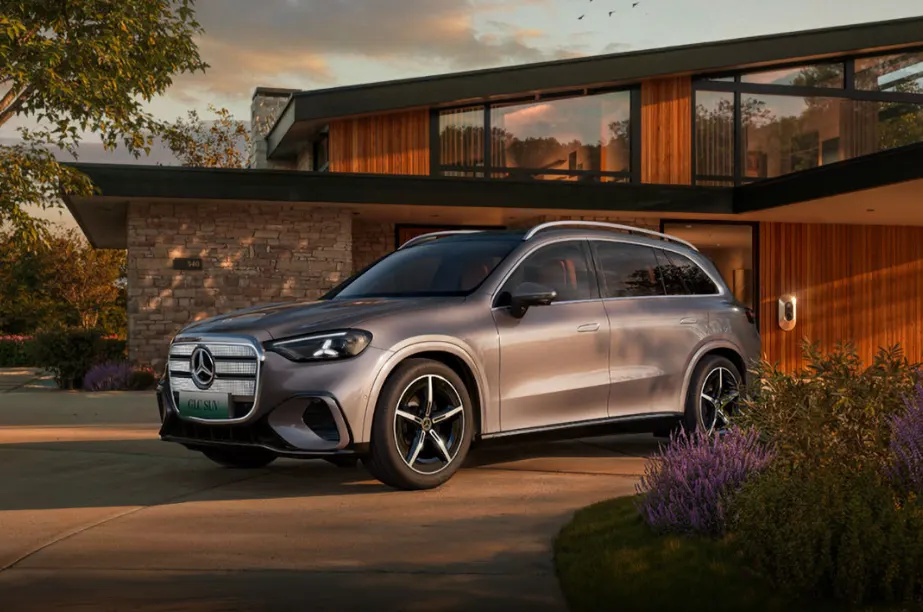 Серебристо-бежевый Mercedes-Benz GLC стоит у современного дома с каменной и деревянной отделкой на закате