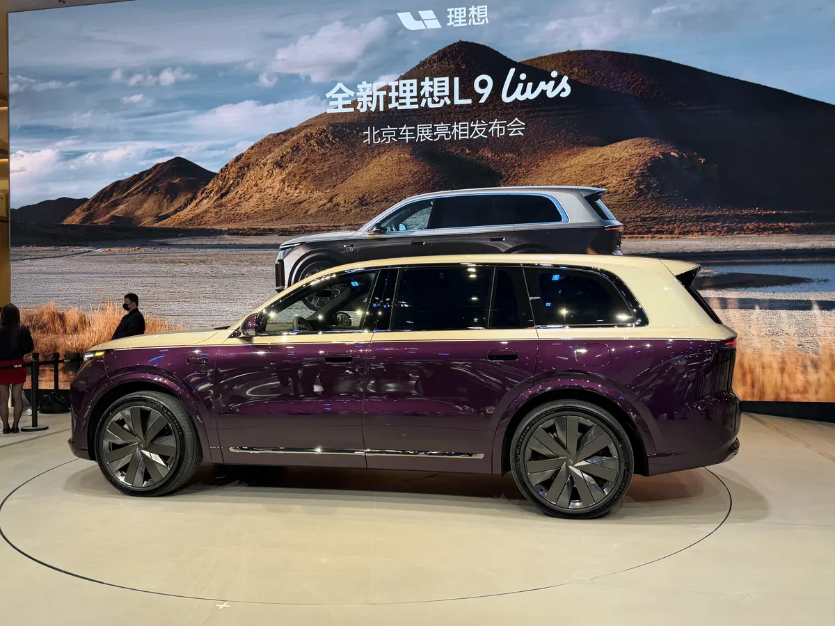 Li Auto L9 Livis сбоку: двухцветный кузов фиолетовый с золотистой крышей, на заднем плане экран с горным пейзажем