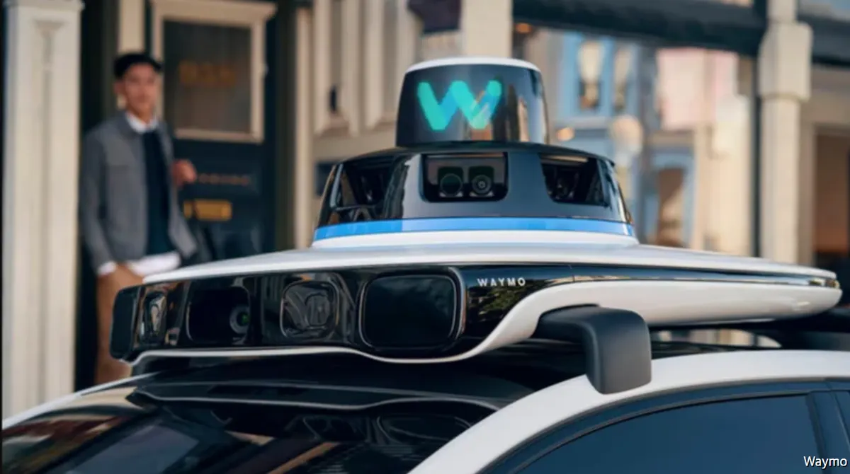 Крыша беспилотного такси Waymo с блоком датчиков и камер, на заднем плане размытый мужчина