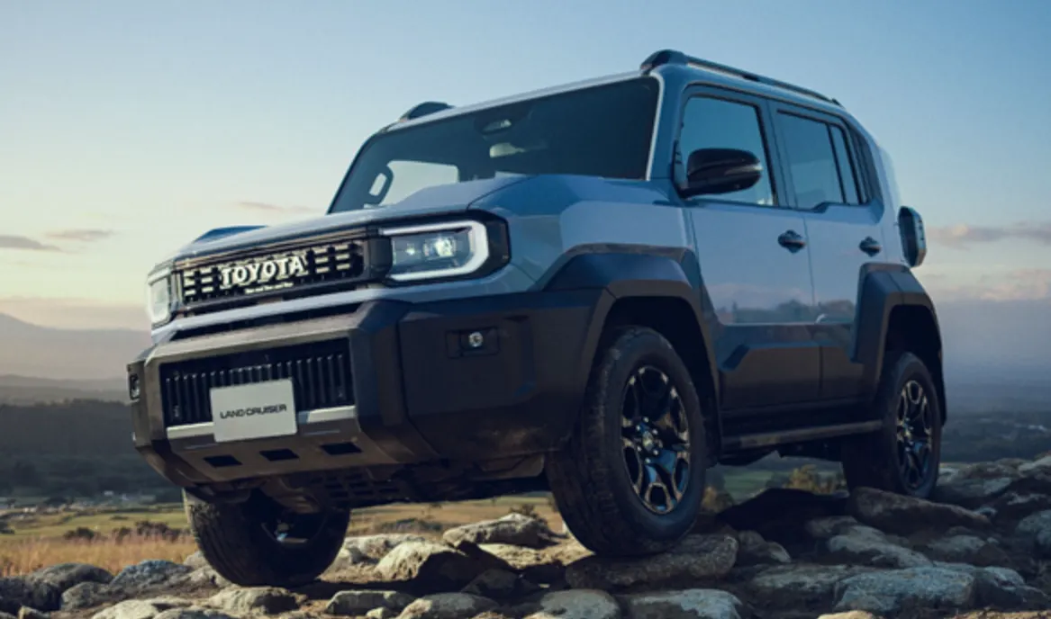 Синий Toyota Land Cruiser FJ с тёмным обвесом стоит на камнях на фоне холмов и закатного неба, вид спереди слева