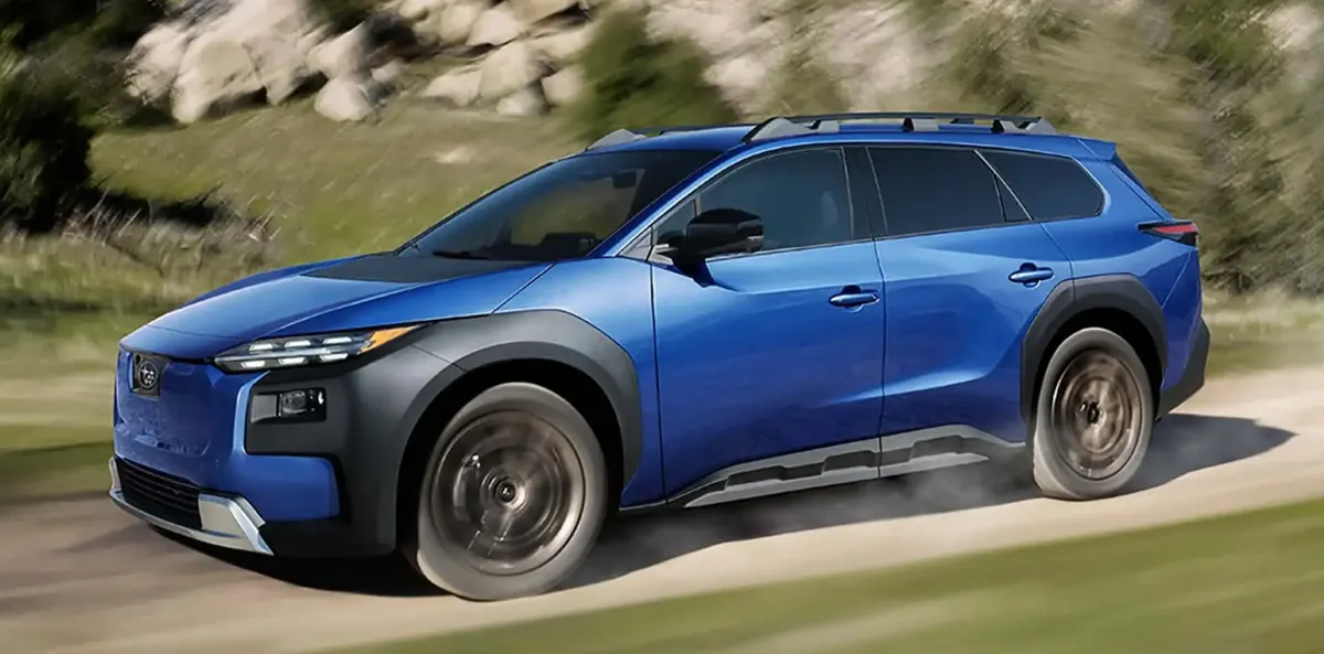 Синий кроссовер Subaru с чёрными пластиковыми накладками арок и рейлингами на крыше едет по грунтовой дороге