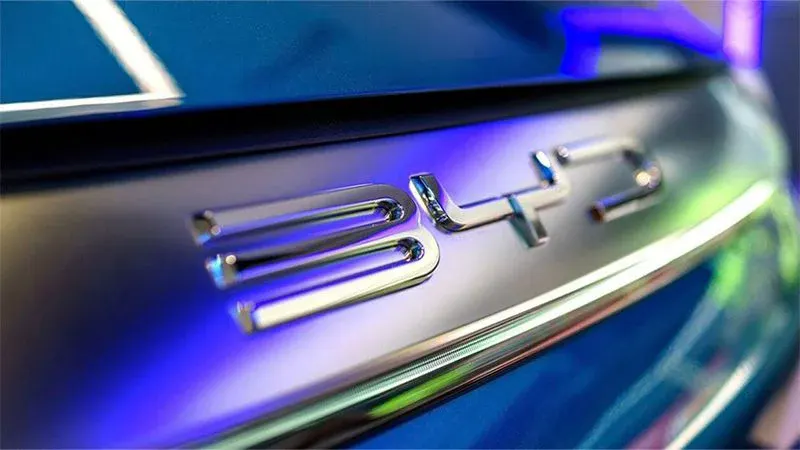 Хромированный логотип BYD на кузове автомобиля крупным планом, подсветка в синих тонах
