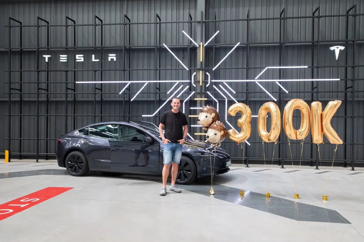 Мужчина у тёмно-серого Tesla Model 3 в салоне с золотыми воздушными шарами «300K» и шарами-ёжиками